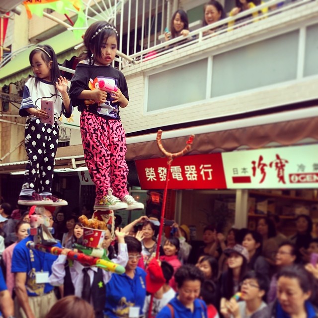 Two girls on poles at the #PiuSik #parade at the #cheungchau #bunfestival. Uh, that costume's a bit modern innit? #hongkong #hk #hkig