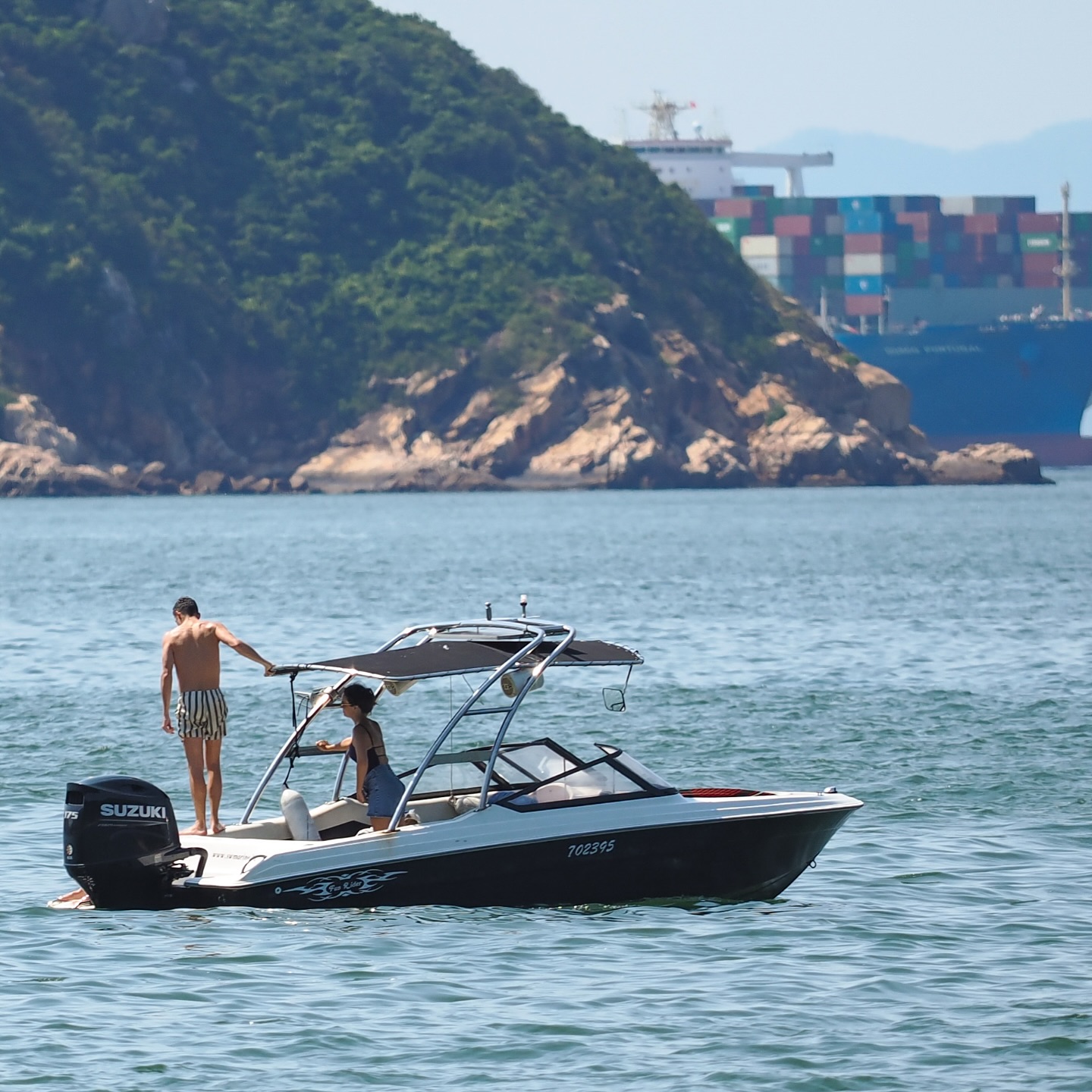 Summer in Hong Kong. A couple take their boat out for a ride while a container ship lurks in the background. hongkong hk hkig summer sea boat containership