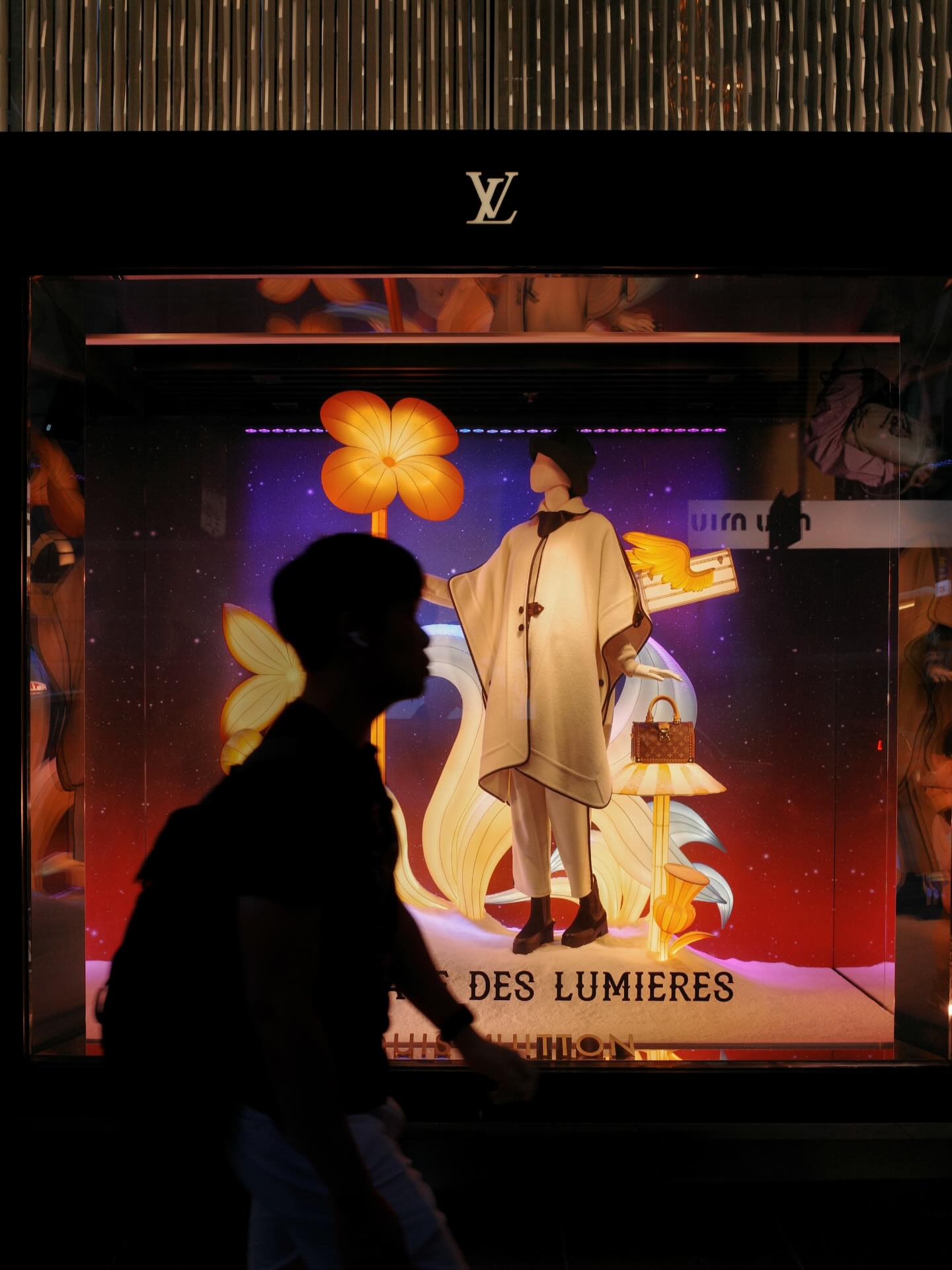 A silhouette of a man walking past a Louis Vuitton storefront in Central, Hong Kong.