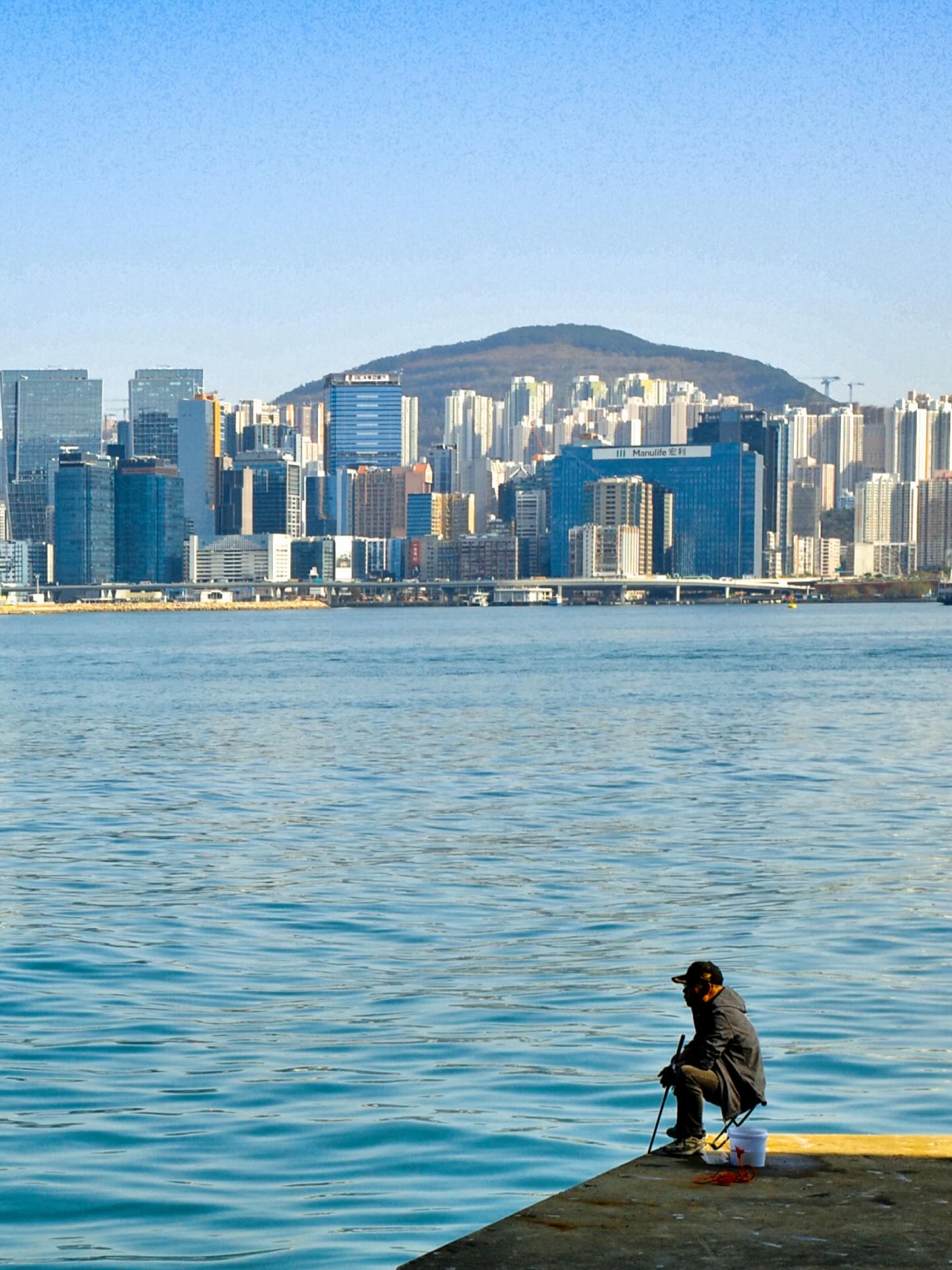 The old man and the sea. A fisherman sits off the newly opened East Coast Boardwalk in North Point, Hong Kong. Kowloon looms on the opposite shore. hongkong hkig fisherman northpoint eastcoastboardwalk
